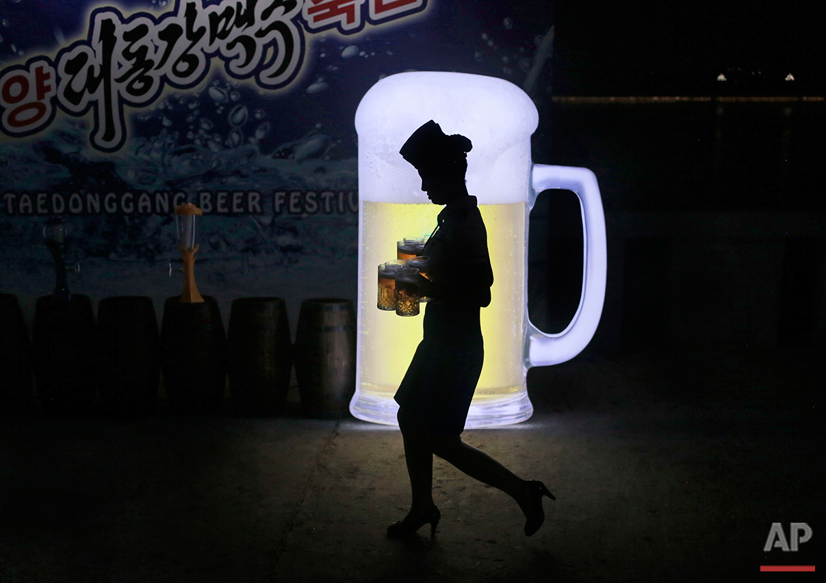  A waitress walks past an advertisement as she carries mugs of beer during Taedonggang Beer Festival in Pyongyang, North Korea, Sunday, Aug. 21, 2016. The festival, the first of its kind in the country, was held as a promotional event for the locally