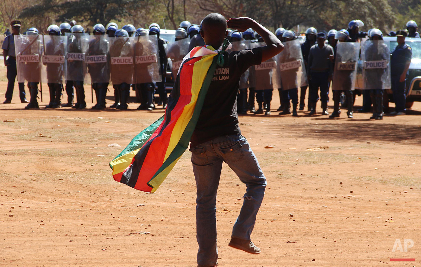  A man wearing a Zimbabwean flag salutes riot police during a protest in Harare, Zimbabwe, on Friday, Aug. 26, 2016. The demonstration organized by opposition political parties calling for reforms, is the first time that the fractured opposition has 