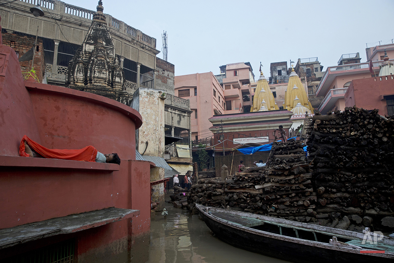  An Indian man sleeps outside a temple as local workers stack woods to be used for funeral pyres at the flooded Manikarnika Ghat in Varanasi, India, Saturday, Aug. 27, 2016. As the mighty Ganges River overflowed its banks this past week following hea