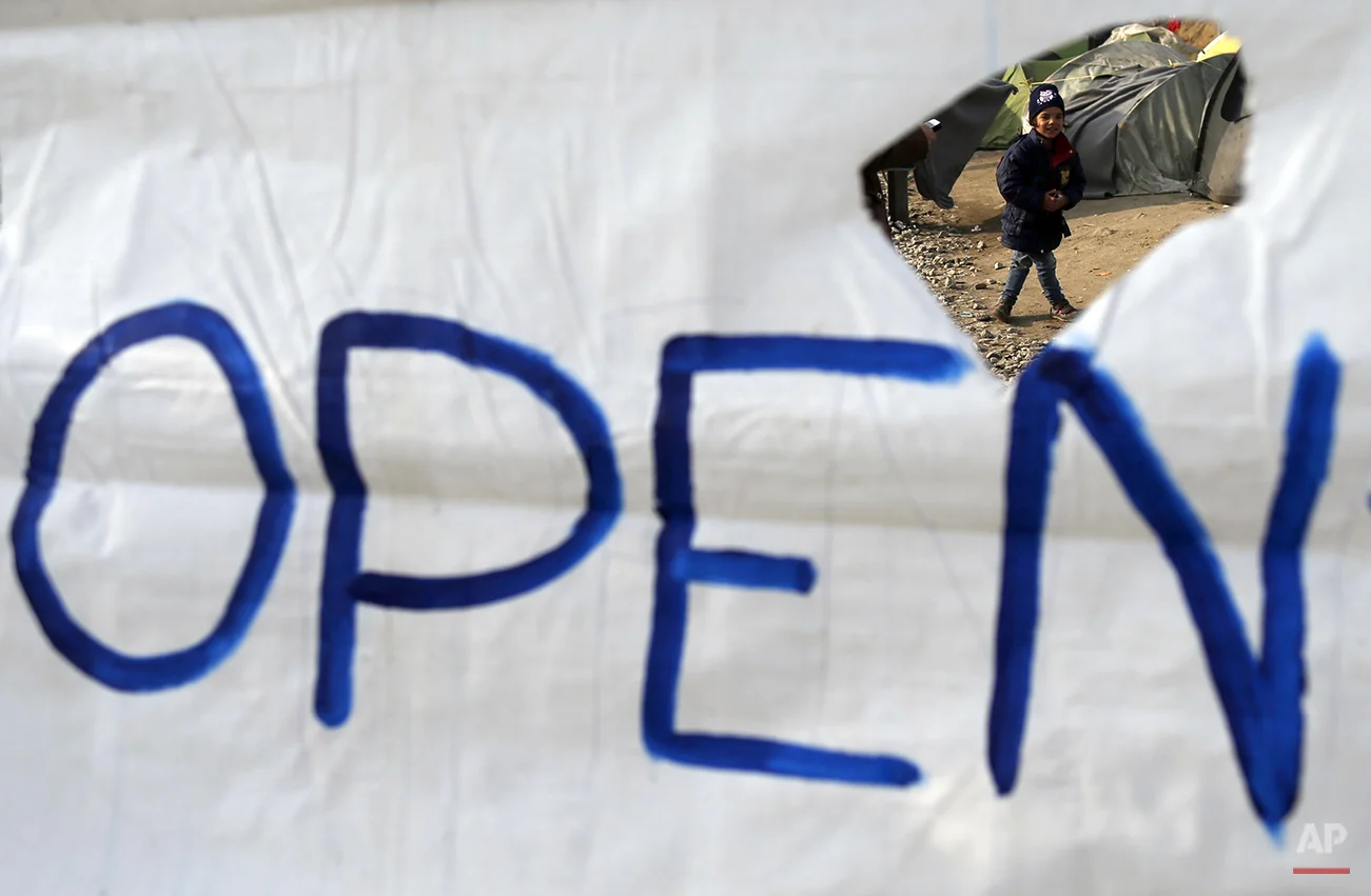  A boy walks behind a banner in a makeshift refugee camp at the northern Greek border point of Idomeni, Greece, Friday, April 1, 2016. More than 50,000 refugees and migrants have been stranded in Greece after Balkan countries closed their borders to 