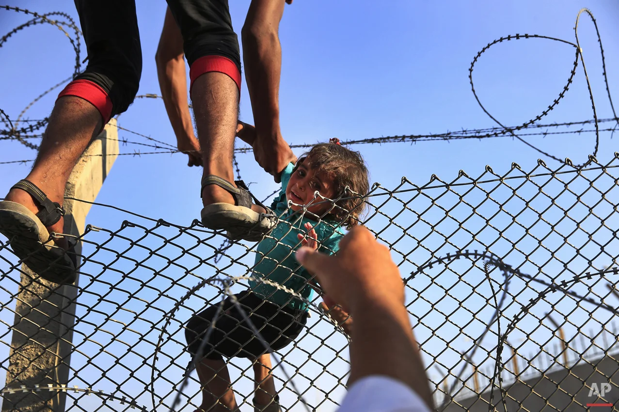 A Syrian refugee carries a baby over the border fence into Turkey from Syria in Akcakale, Sanliurfa province, southeastern Turkey, Sunday, June 14, 2015. Thousands of Syrians cut through a border fence and crossed over into Turkey on Sunday, fleeing intense fighting in northern Syria between Kurdish fighters and jihadis.The flow of refugees came as Syrian Kurdish fighters closed in on the outskirts of a strategic Islamic State-held town on the Turkish border. (AP Photo/Lefteris Pitarakis)