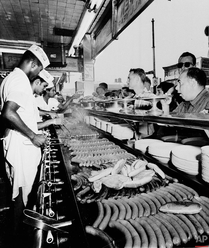 Nathan's Famous hot dogs are cooked on the grill as customers line up at Coney Island in Brooklyn, New York, on Sept. 10, 1958. (AP Photo)