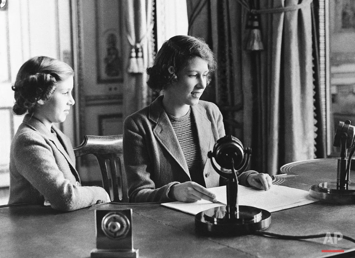 Performing one of the many public duties she will be called on, as a member of the Royal House, to fulfill as she grows older, Princess Elizabeth, center, 11-year-old heiress apparent to the British throne, is shown as she made her rapid debut, broadcasting a three-minute speech to British girls and boys evacuated overseas, Oct. 22, 1940, London, England. She is joined in bidding good-night to her listeners by her sister, Princess Margaret Rose.