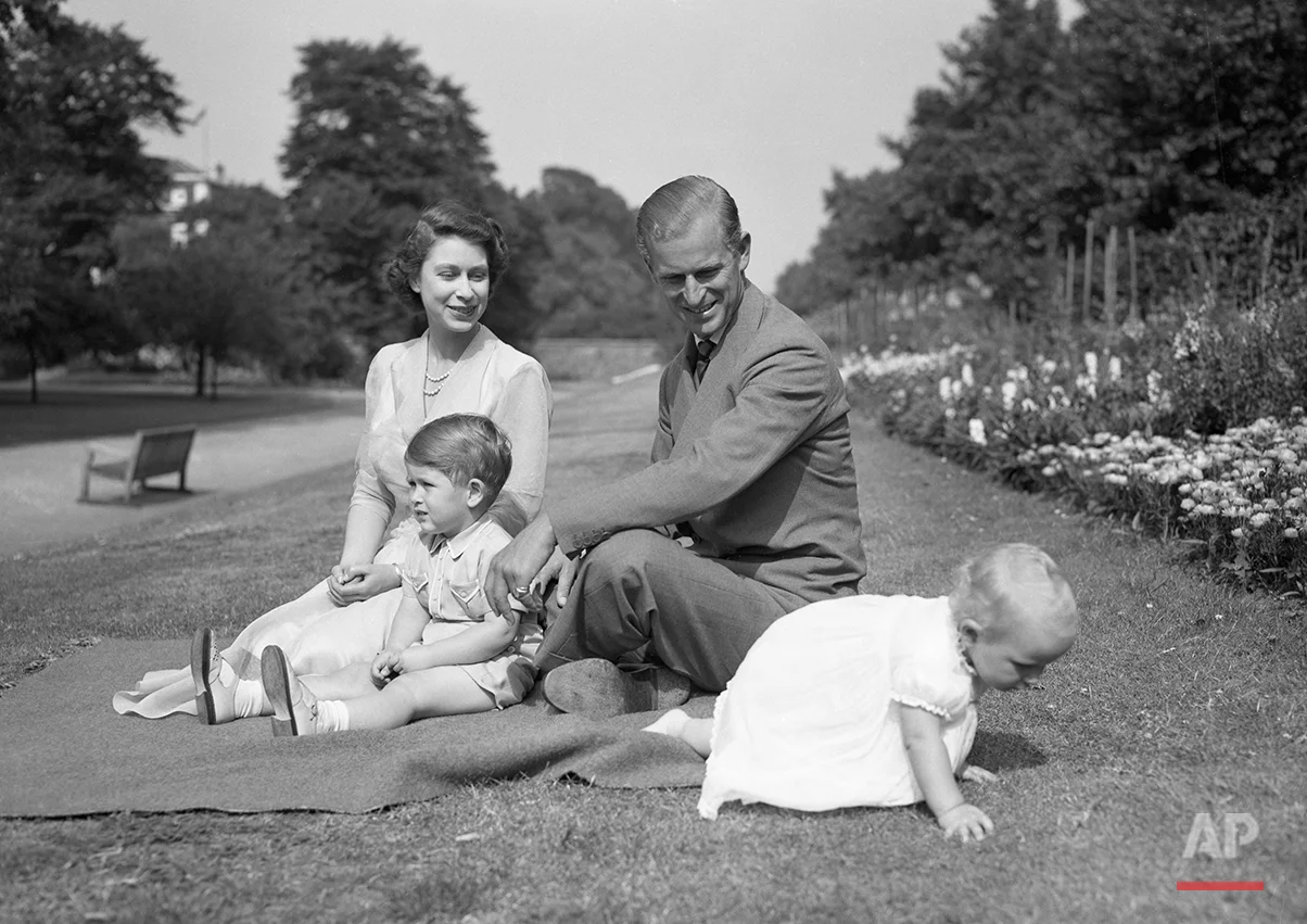 Princess Elizabeth sits with her husband Prince Philip, the Duke of Edinburgh, and Prince Charles as they watch Princess Anne try to crawl away at their London residence, Clarence House, August 8, 1951. (AP Photo/Worth)