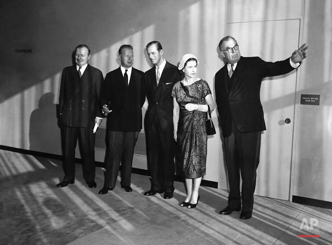 General Assembly President Sir Leslie Munro points to large windows and view from the Security Council chamber as Britain's royal couple tours United Nations headquarters in New York City on Oct. 21, 1957. Left to Right, are: Britain's Selwyn Lloyd, U.N. Secretary General Dag Hammarskjold, Prince Philip, Queen Elizabeth II and Sir Leslie. Sun coming through windows casts shadows on the group. (AP Photo)