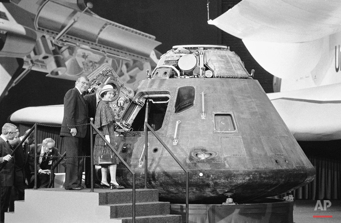 Britain's Queen Elizabeth II looks inside the Apollo 14 command module, a spaceship that visited the Moon in February 1971, during her tour of Rockwell International plant on Monday, Feb. 28, 1983 in Downey, Calif. Guiding the Queen's tour is Rockwell board chairman Robert Anderson, left, and Rockwell North American Space Operations President George Jeffs, background. (AP Photo)