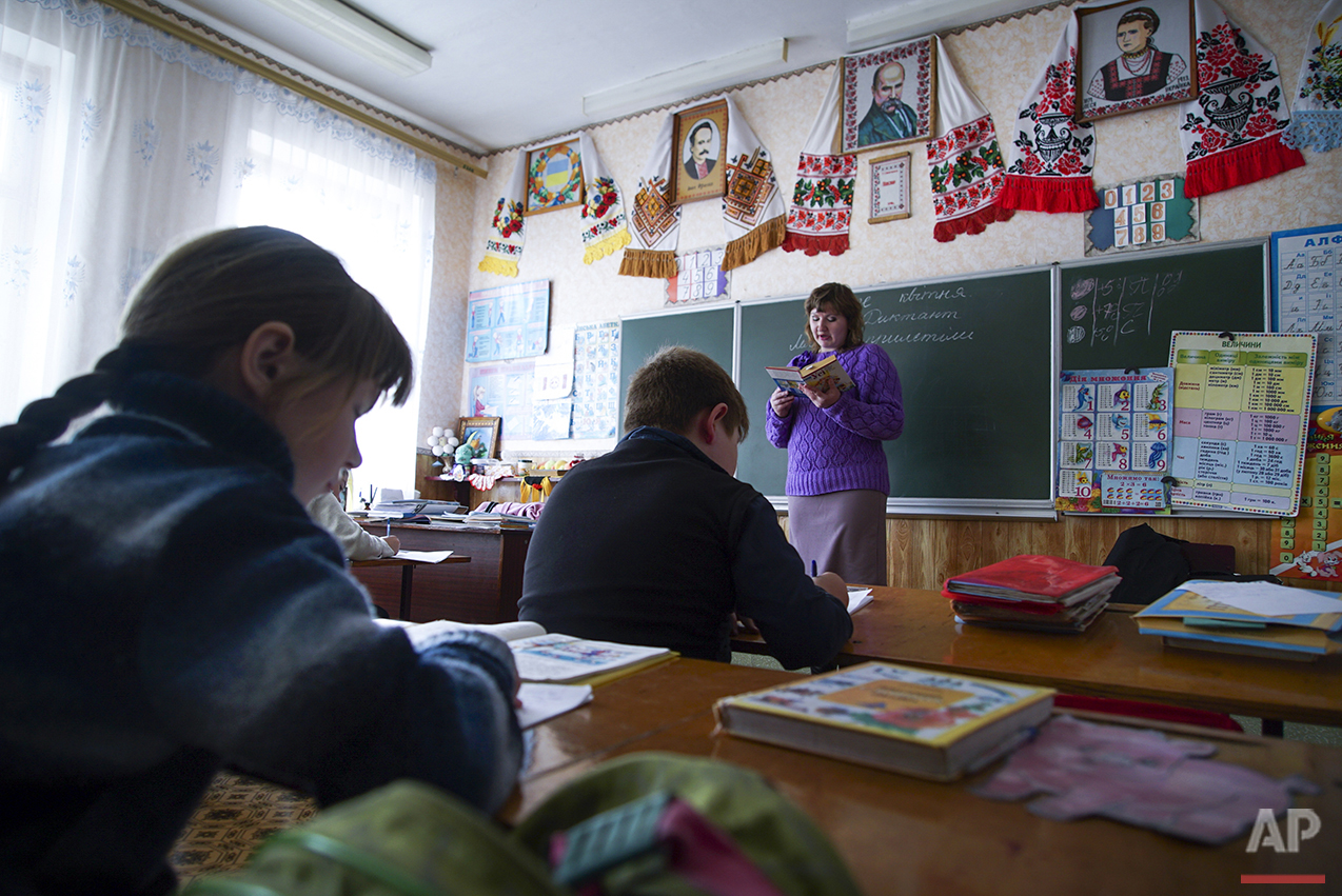  In this photo taken on Tuesday, April  5, 2016, teacher Natalya Stepanchuk, background center, reads, while children write during a lesson in a school in Zalyshany, 53 km (32 miles) southwest of the destroyed reactor of the Chernobyl plant, Ukraine.