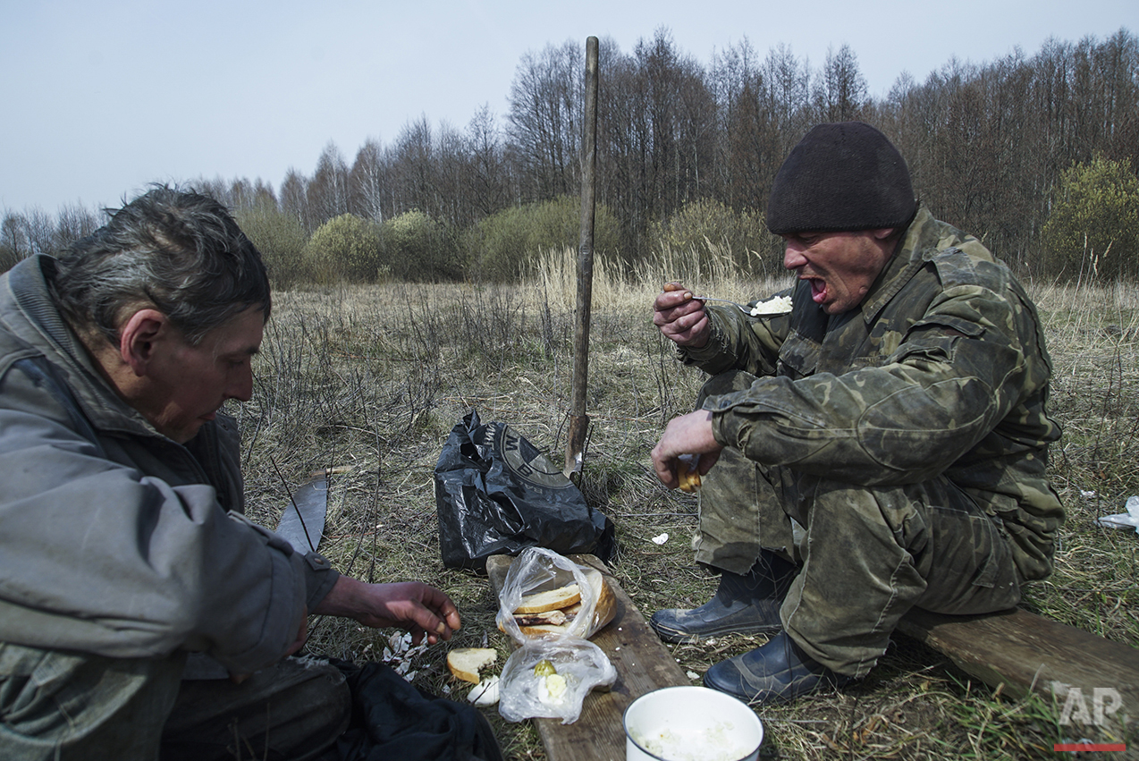  In this photo taken on Tuesday, April  5, 2016, former fireman Volodymir, 50, right, and his friend Andryi, 44, have lunch with food placed on a piece of wood taken from a local forest, believed still to be contaminated by fallout from the world's w