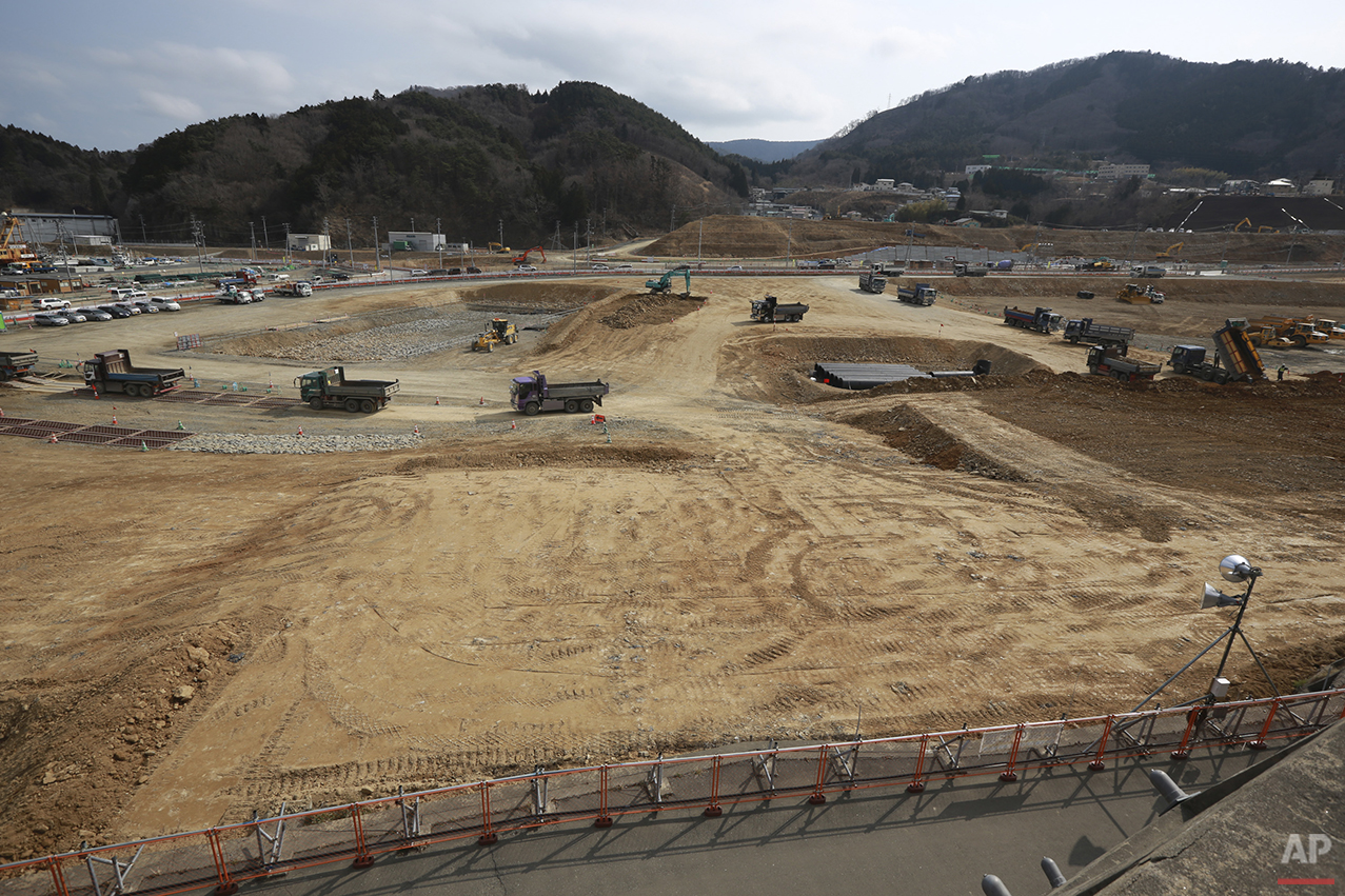  In this Saturday, March 5, 2015 photo, trucks wait in queue to dump soils in the tsunami and earthquake destroyed town of Onagawa, Miyagi Prefecture, northern Japan. Five years after the disaster, construction work is clearly underway but far from d