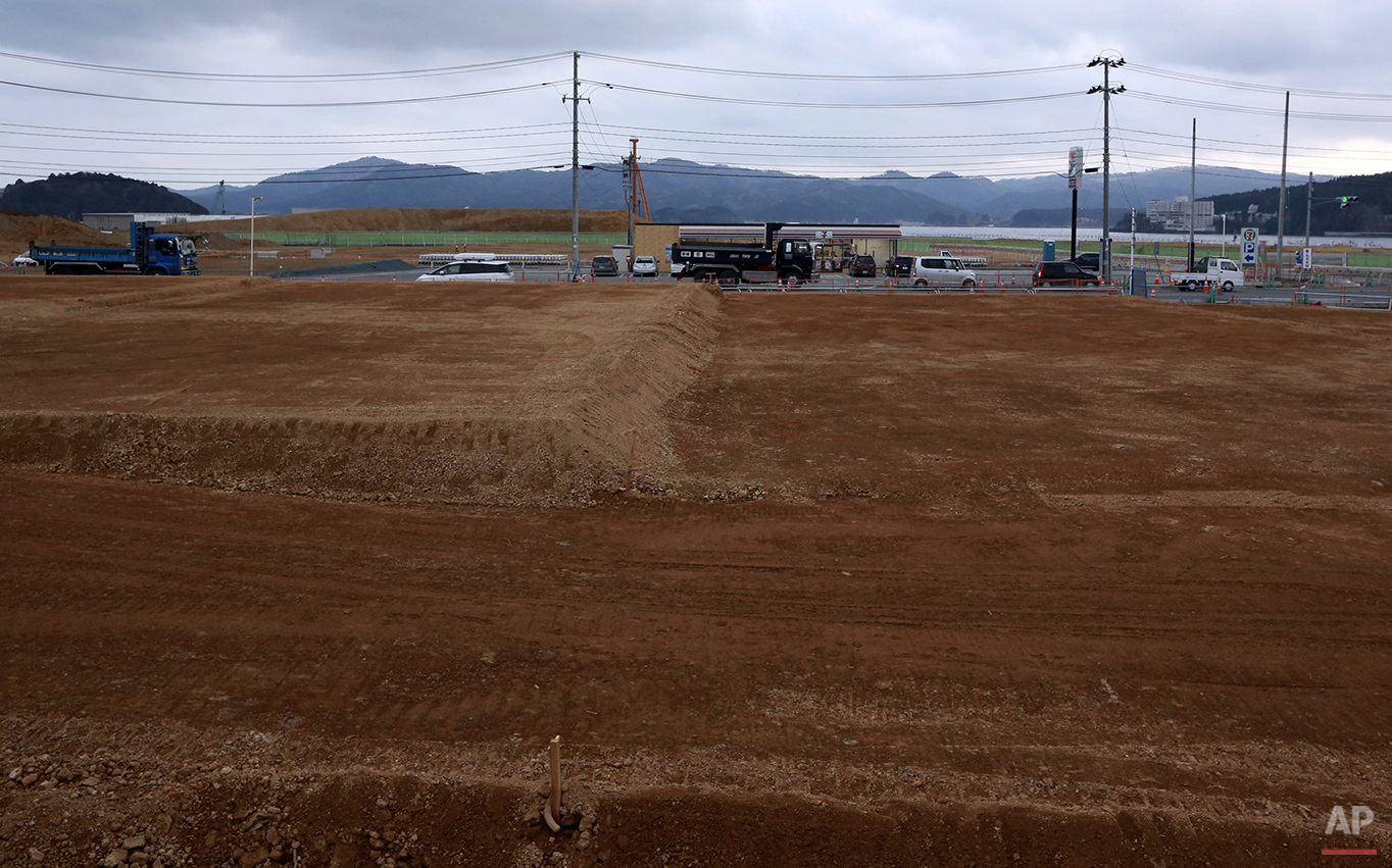  In this Saturday, March 5, 2016 photo, trucks and cars drive through the leveled city of Minamisanriku, Miyagi Prefecture, northern Japan. Five years after the disaster, construction work is clearly underway but far from done. Rebuilt roads stretch 