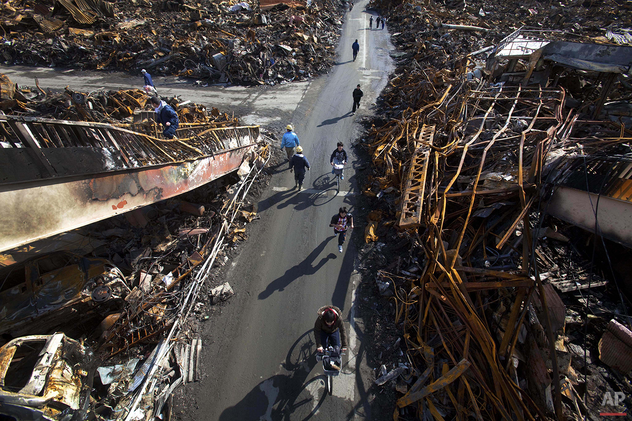  In this March 17, 2011 photo, Japanese residents of Kesennuma, Miyagi Prefecture, northeastern Japan, are seen from a destroyed pedestrian bridge, passing through a road that was cleared by a bulldozer through the ruins of the city, six days after t