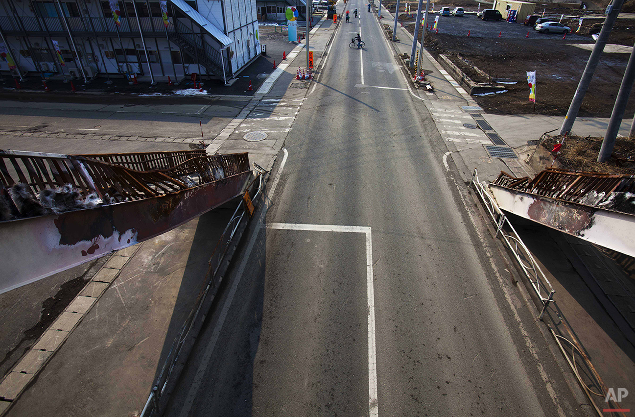  In this Feb. 23, 2012 photo, Japanese residents of Kesennuma, Miyagi Prefecture, northern Japan, are seen from a destroyed pedestrian bridge, crossing a road in the destroyed part of the city, almost one year after the March 11, 2011 tsunami hit the