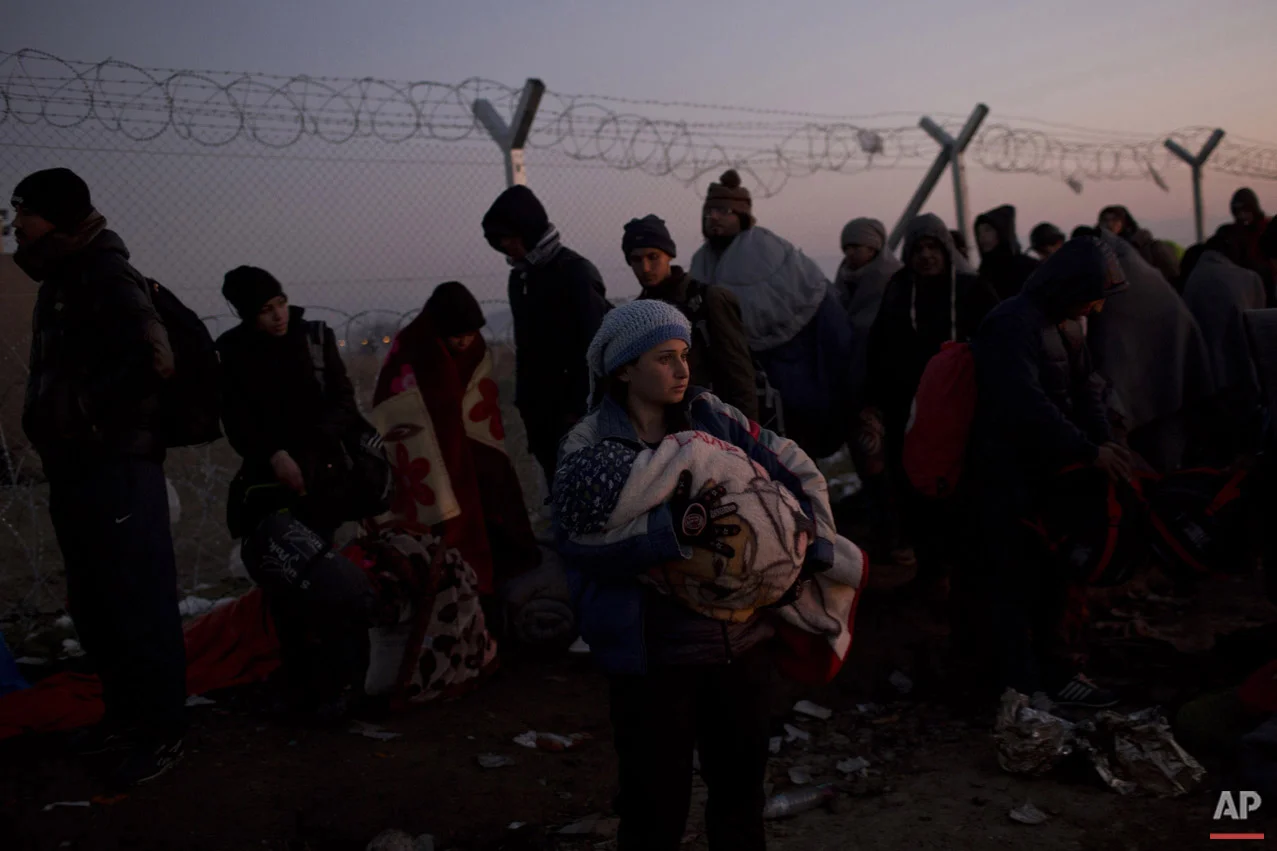 A woman holds her baby as she waits with other refugees in front of the wire fence that separates the Greek side from the Macedonian one, to be allowed to cross into Macedonia, at the northern Greek border station of Idomeni, Sunday, Dec. 6, 2015.