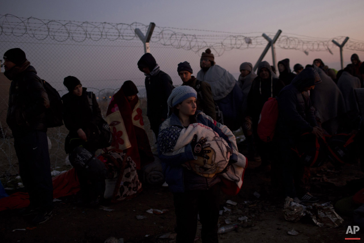  A woman holds her baby as she waits with other refugees in front of the wire fence that separates the Greek side from the Macedonian one, to be allowed to cross into Macedonia, at the northern Greek border station of Idomeni, Sunday, Dec. 6, 2015.  