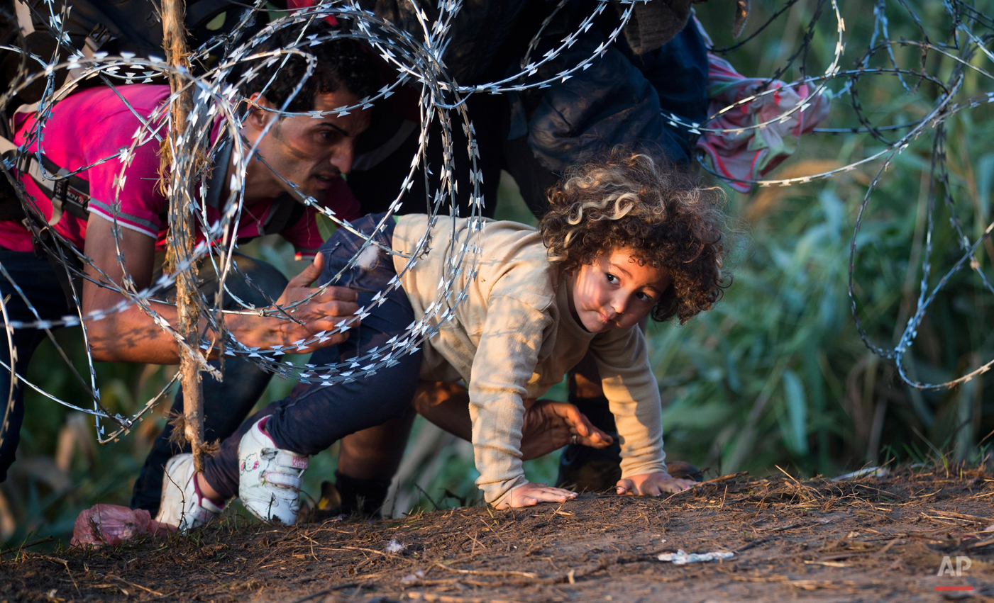  In this Thursday, Aug. 27, 2015 photo, a child is helped cross from Serbia to Hungary through the barbed wire fence near Roszke, southern Hungary. Round the clock, thousands of refugees cross daily along the approximately 110-mile (175-kilometer) bo