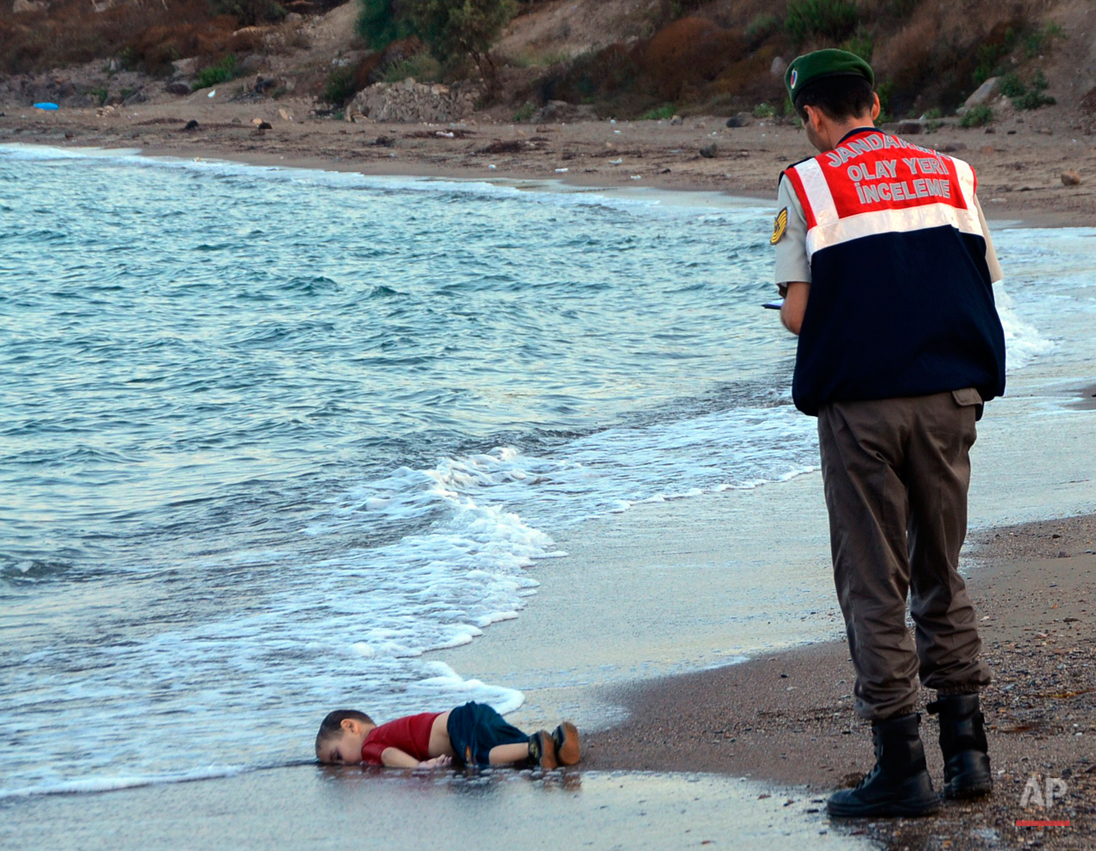  A paramilitary police officer investigates the scene before carrying the lifeless body of 3-year-old Aylan Kurdi from the sea shore, near the beach resort of Bodrum, Turkey, early Wednesday, Sept. 2, 2015. A number of migrants are known to have died