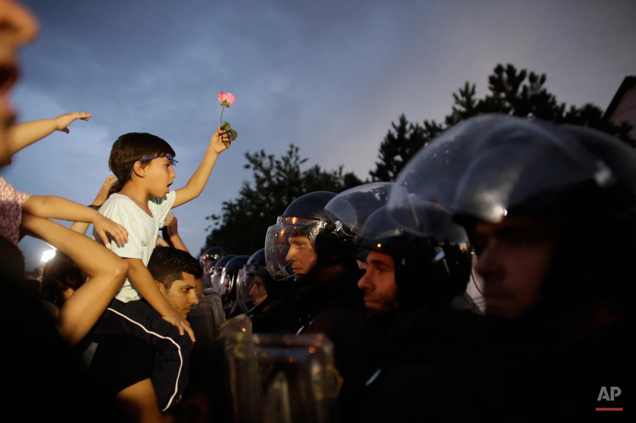 A boy with a flower sits on the shoulders of a man as a group of refugees and supporters face Slovenian police blocking the entrance to Slovenia at the border crossing in the Croatian village of Harmica, Friday, Sept. 18, 2015. (AP Photo/Markus Schreiber)