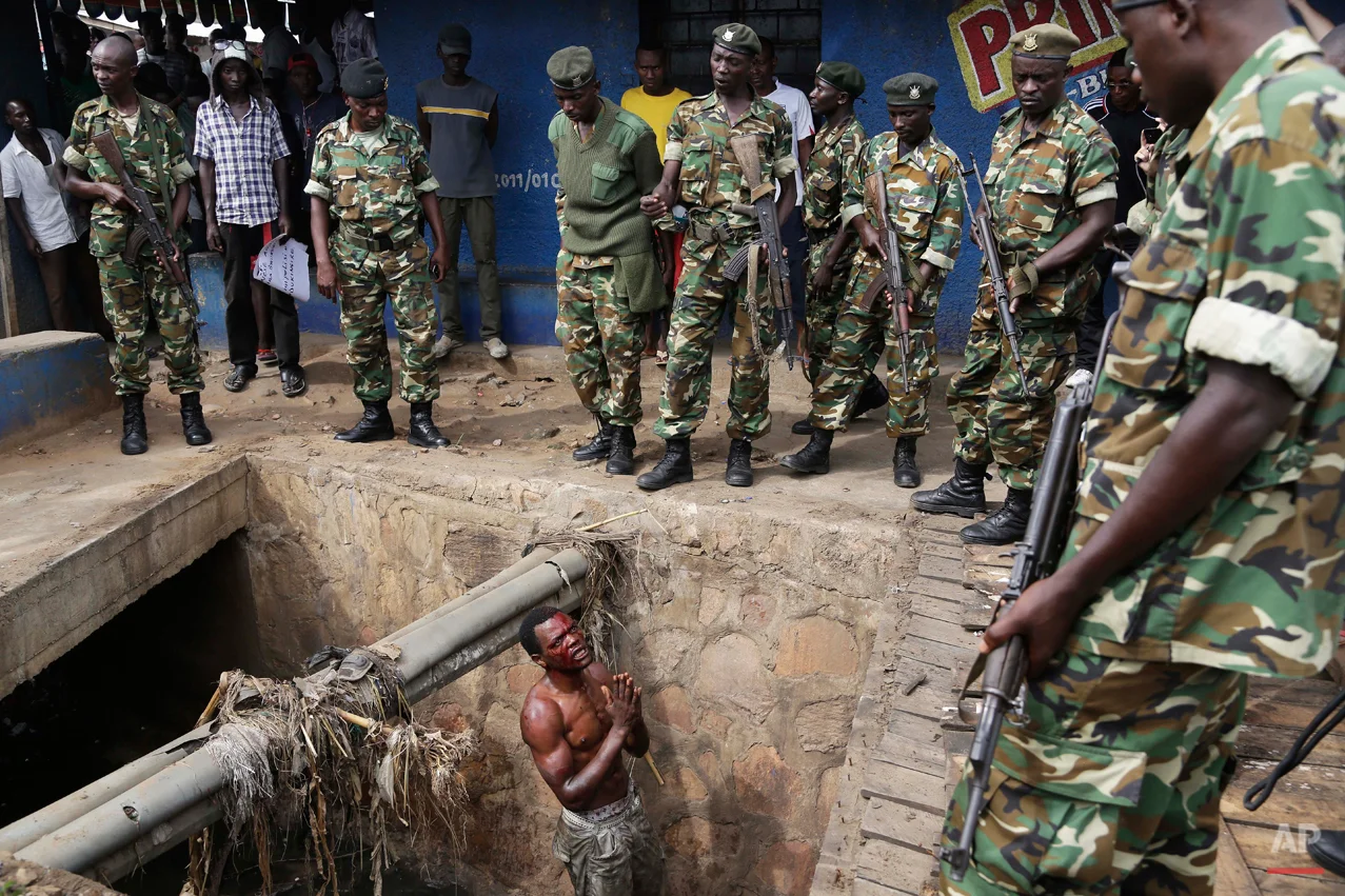 Jean Claude Niyonzima, a suspected member of the ruling party's Imbonerakure youth militia, pleads with soldiers to protect him from a mob of demonstrators after he came out of a sewer in the Cibitoke district of Bujumbura, Burundi, Thursday, May 7, 2015. (AP Photo/Jerome Delay)