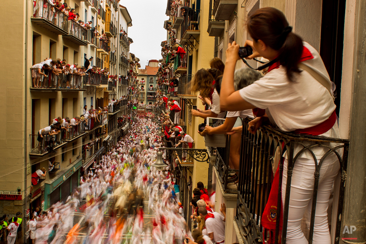  People watch as El Tajo y La Reina fighting bulls and revelers run during the running of the bulls, at the San Fermin festival, in Pamplona, Spain, Wednesday, July 8, 2015. Revelers from around the world arrive to Pamplona every year to take part in