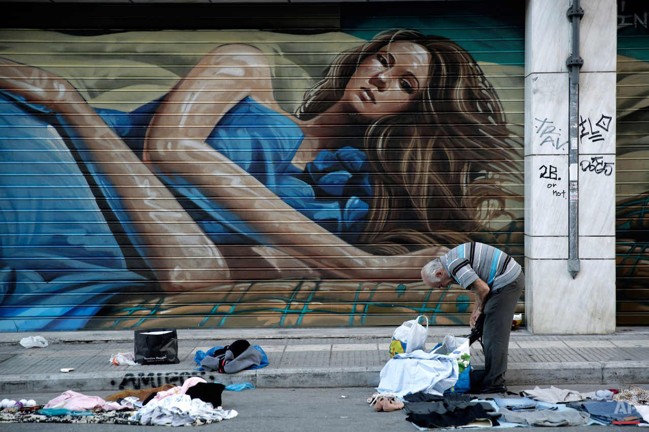  In this Wednesday, May 13, 2015 photo, a street vendor collects his clothes outside the shutters of a shop in central Athens. Greece, which is in the midst of protracted bailout talks with creditors, is now officially in recession again according to
