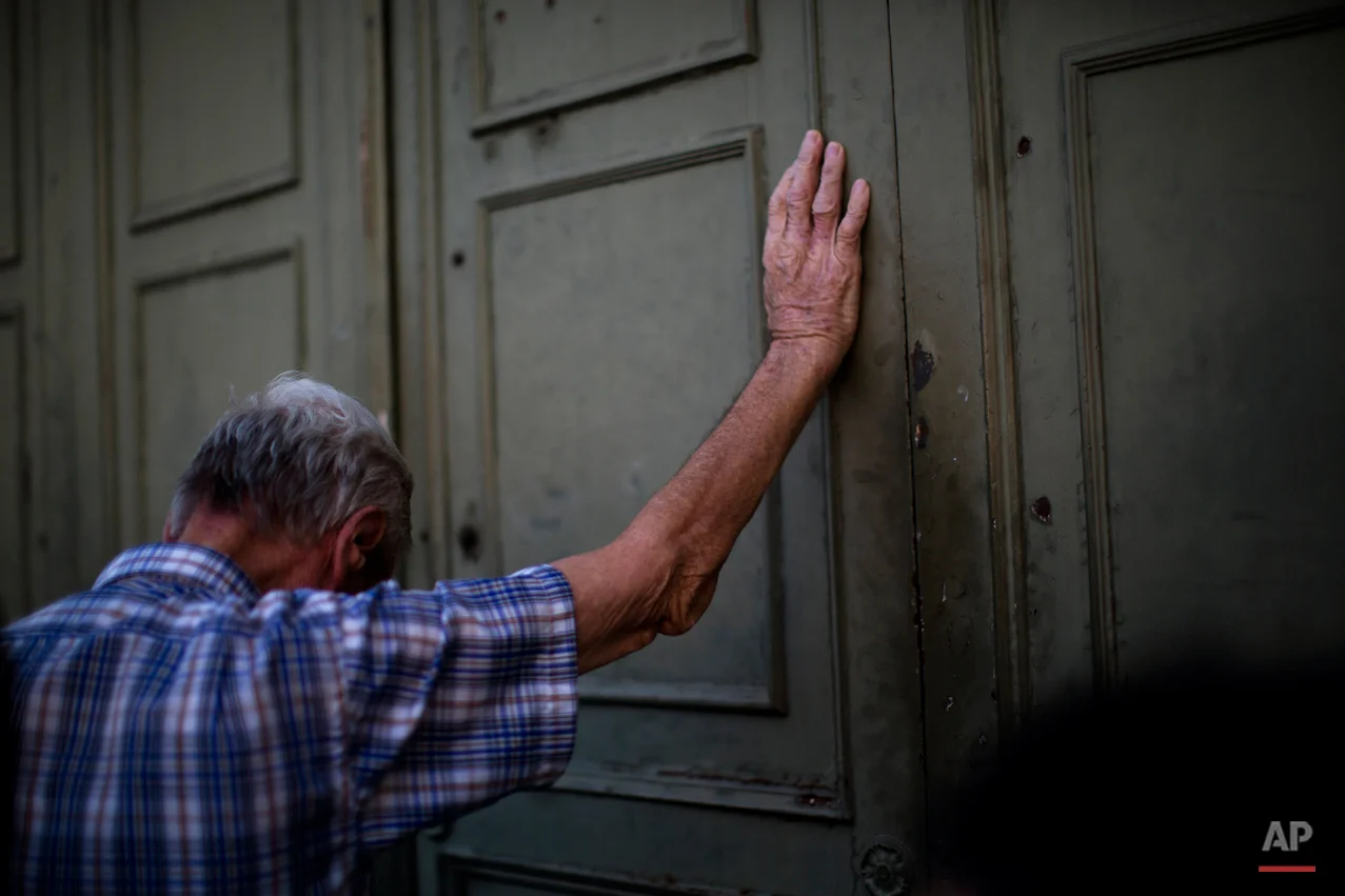 A pensioner leans against the main gate of the national bank of Greece as he waits to withdraw a maximum of 120 euros ($134) for the week in Athens in central Athens, Tuesday, July 7, 2015. (AP Photo/Emilio Morenatti)