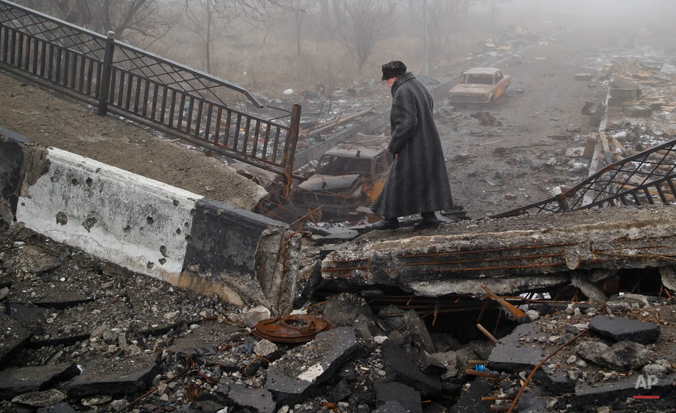 In this Sunday, March 1, 2015, photo, an elderly woman walks across a destroyed bridge, which has collapsed over the road to the airport, the scene of heavy fighting, in Donetsk, Ukraine. (AP Photo/Vadim Ghirda)