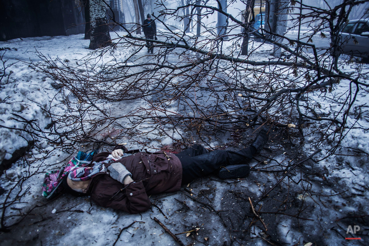  A person walk near the remains of a man lying near a bus stop that was damaged in shelling in Donetsk, eastern Ukraine, Tuesday, Jan. 20, 2015. At least three civilians were killed in shelling Tuesday in eastern Ukraine as fighting continued between