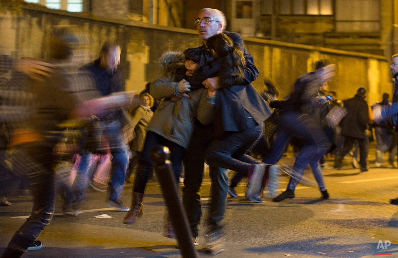  A man carries two children after panic broke out among mourners who payed their respect at the attack sites at restaurant Le Petit Cambodge (Little Cambodia) and the Carillon Hotel in Paris, Sunday, Nov. 15, 2015. (AP Photo/Peter Dejong) 