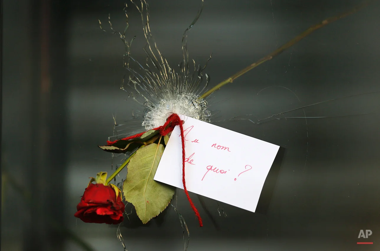A message that reads: "In the name of what?" and a rose is placed through a bullet hole in a window at the restaurant on Rue de Charonne, Paris, Sunday, Nov. 15, 2015, where attacks took place on Friday. The Islamic State group claimed responsibility for Friday's attacks on a stadium, a concert hall and Paris cafes that left more than 120 people dead and over 350 wounded. (AP Photo/Frank Augstein)
