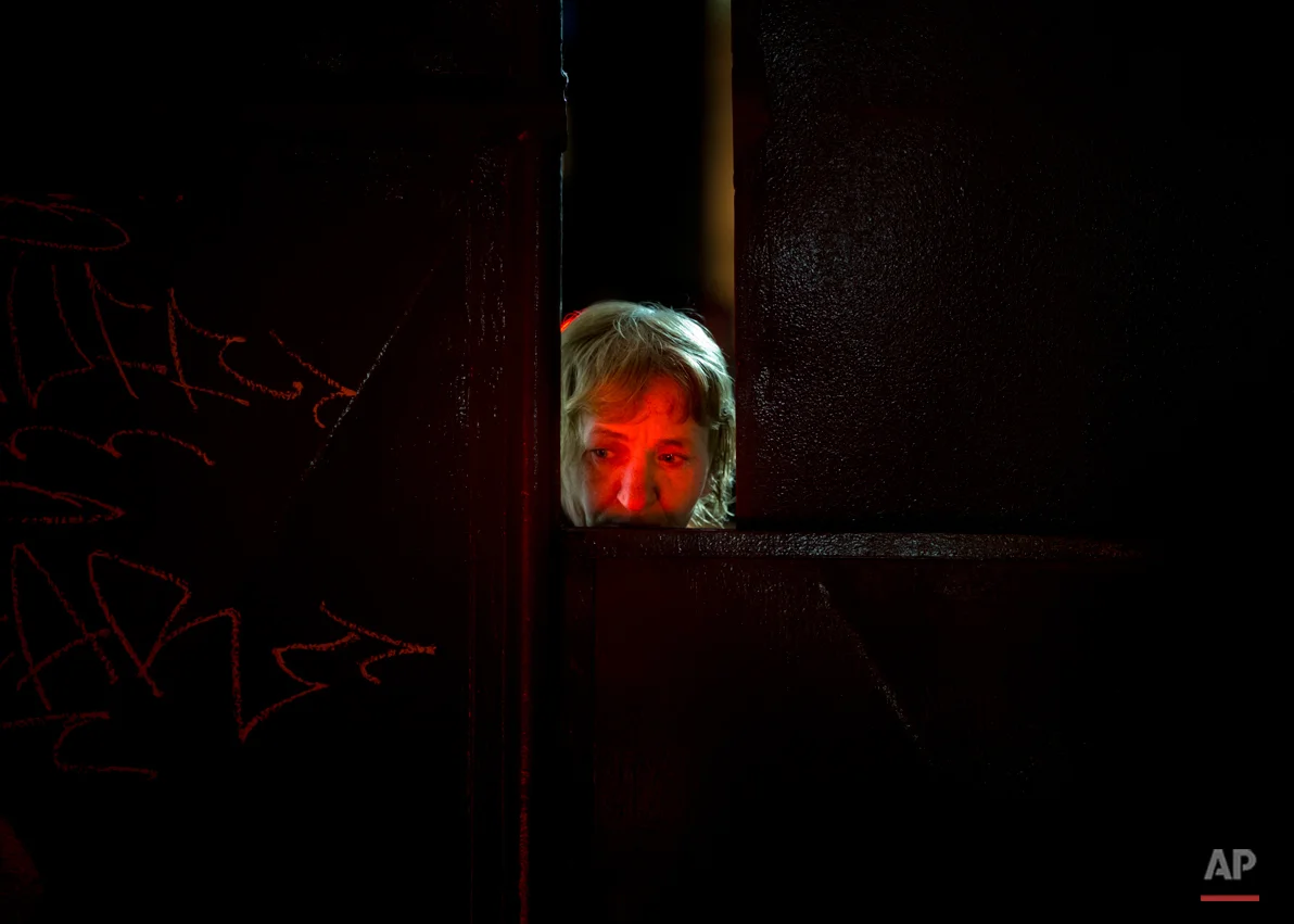 A woman face is lit by candles placed outside the Colectiv nightclub as she peers from behind the metal gate leading to the club in Bucharest, Romania, Monday, Nov. 2, 2015. The owners of the Colectiv nightclub were questioned by prosecutors Monday in connection with a fire that engulfed a nightclub Friday night, causing a stampede to a single exit door of the basement club and leaving tens of people dead and many more injured. (AP Photo/Vadim Ghirda)