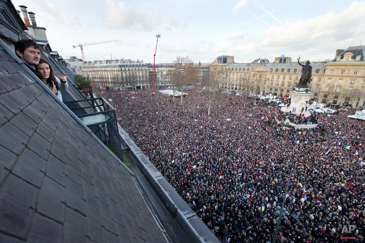  People watch from their roof-top apartment as some thousands of people gather at Republique square in Paris, France, Sunday, Jan. 11, 2015. Thousands of people began filling France's iconic Republique plaza, and world leaders converged on Paris in a