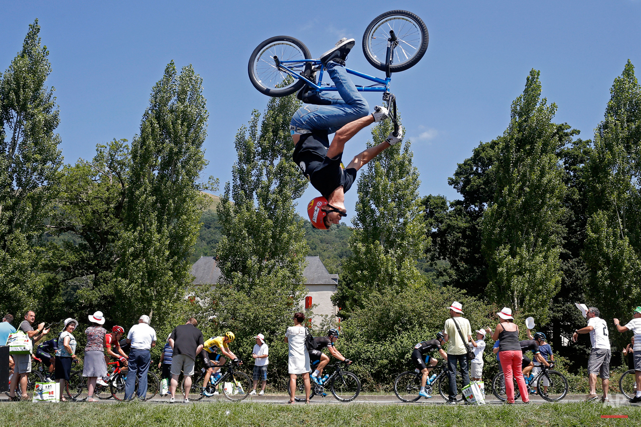  In this Tuesday, July 14, 2015 photo, a man performs a BMX bike stunt as the pack with Britain's Christopher Froome, wearing the overall leader's yellow jersey, passes during the tenth stage of the Tour de France cycling race over 167 kilometers (10