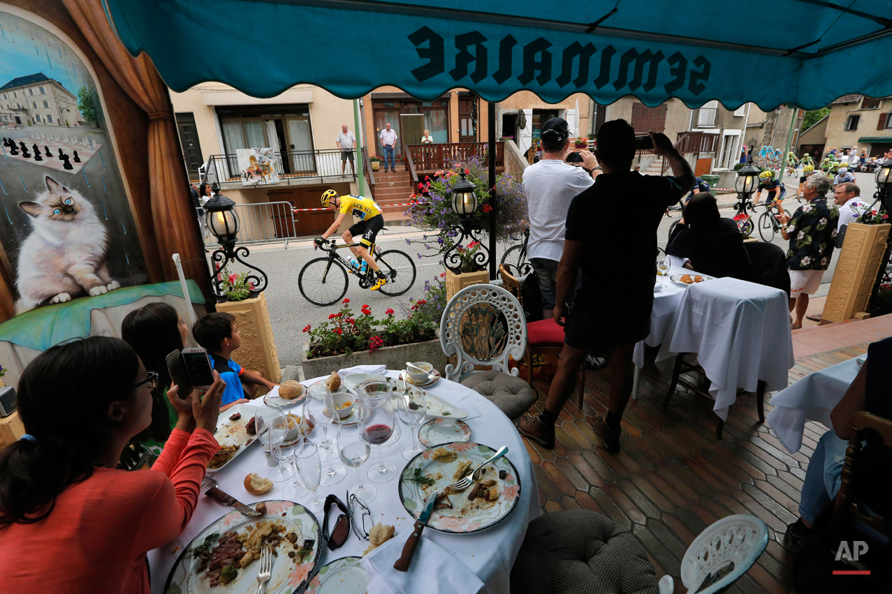  In this Thursday, July 23, 2015 file photo clients watch from the terrace of a restaurant as the pack with Britain's Chris Froome, wearing the overall leader's yellow jersey, passes during the eighteenth stage of the Tour de France cycling race over
