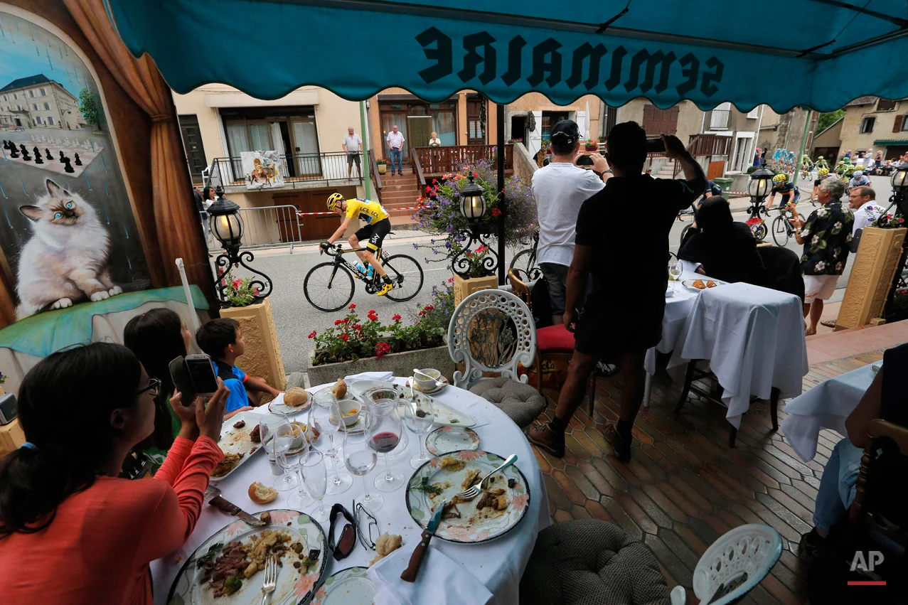 In this Thursday, July 23, 2015 file photo clients watch from the terrace of a restaurant as the pack with Britain's Chris Froome, wearing the overall leader's yellow jersey, passes during the eighteenth stage of the Tour de France cycling race over 186.5 kilometers (115.9 miles) with start in Gap and finish in Saint-Jean-de-Maurienne, France. (AP Photo/Christophe Ena)