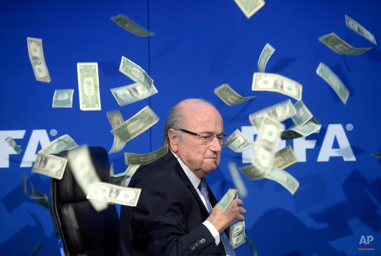  In this Wednesday, Aug. 5, 2015 photo, FIFA president Sepp  Blatter is photographed while banknotes thrown by British comedian Simon Brodkin hurtle through the air during a press conference following the extraordinary FIFA Executive Committee at the