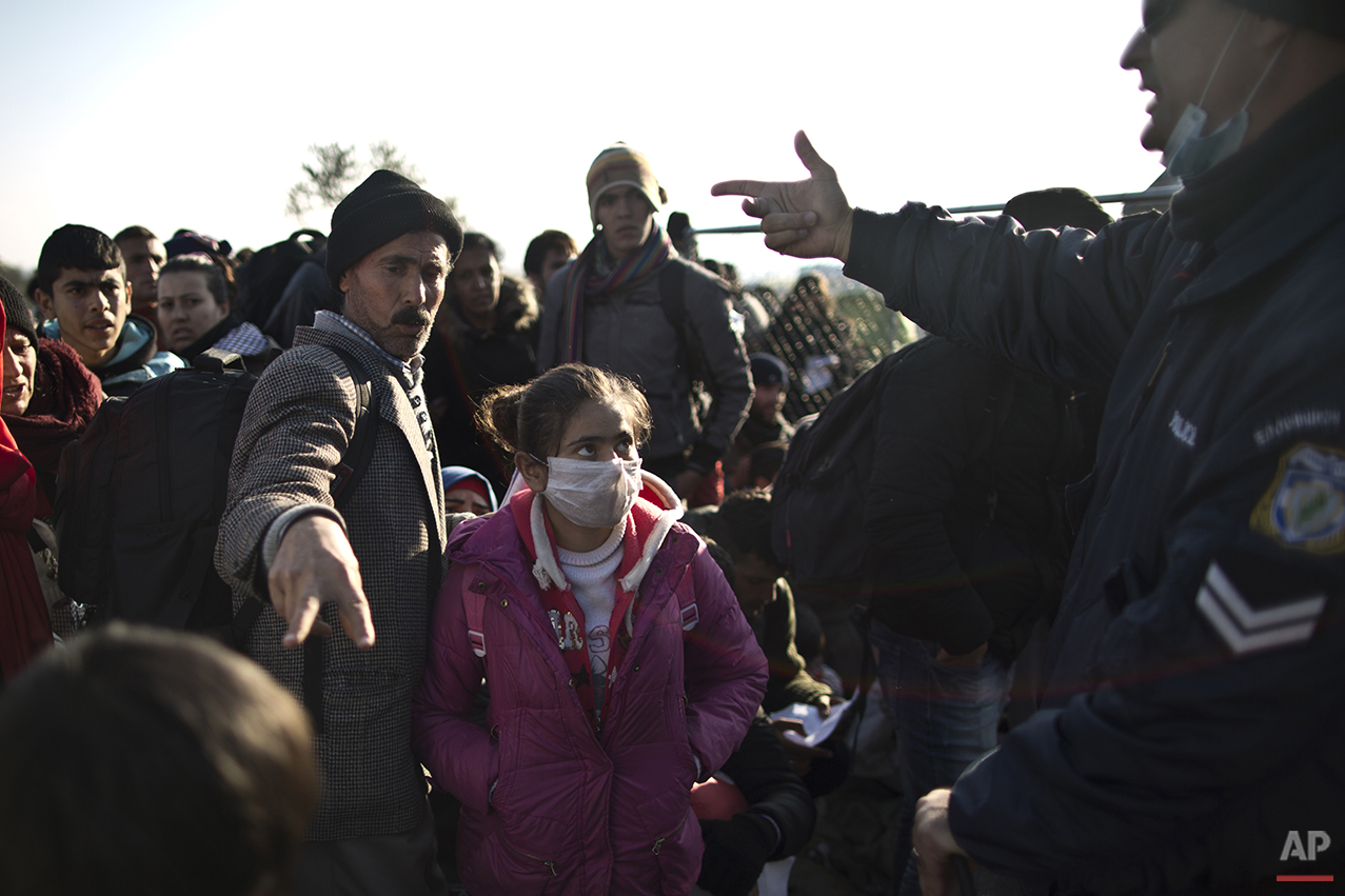  In this Saturday, Dec. 5, 2015 photo, Yazidi refugee Samir Qasu, 45, center, from Sinjar, Iraq, and his  daughter Dunia, 13, gestures to a Greek police officer while he and his family and other refugees and migrants wait to be permitted to cross the