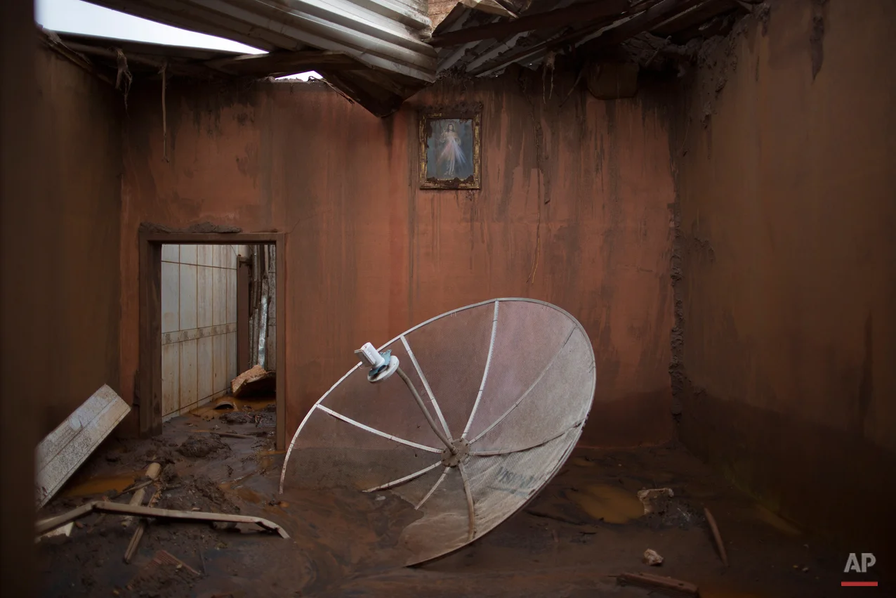  In this Nov. 23, 2015 photo, a satellite dish sits amid debris in a home destroyed when dams of an iron ore mine burst in early November, causing a mudslide, in the village of Bento Rodrigues, Brazil. The village, in the central state of Minas Gerai