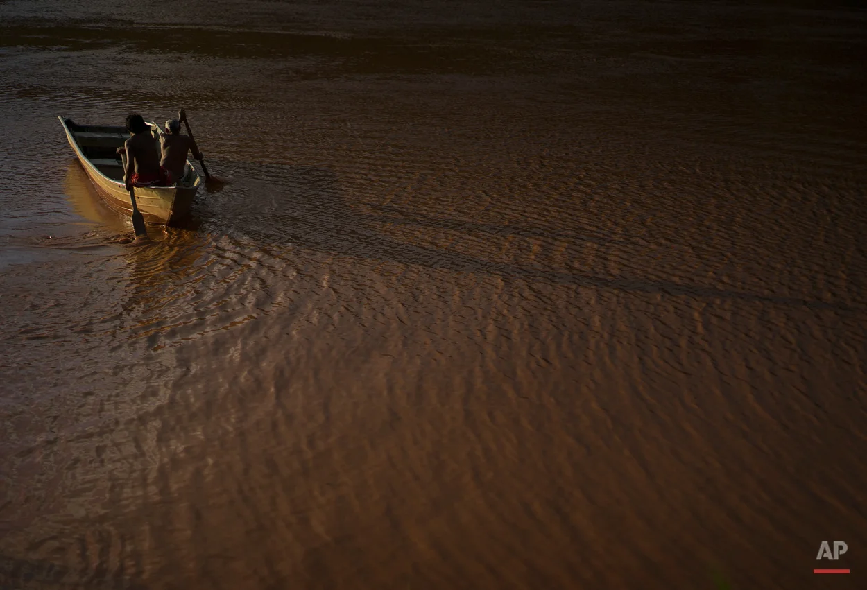  In this Nov. 22, 2015 photo, Ererre, left center, and Jose Cecilio Damasceno, both of the Krenak people, row their boat on the Doce River, polluted by a mix of residues from a dam that burst in early November, in Resplendor, Minas Gerais state, Braz