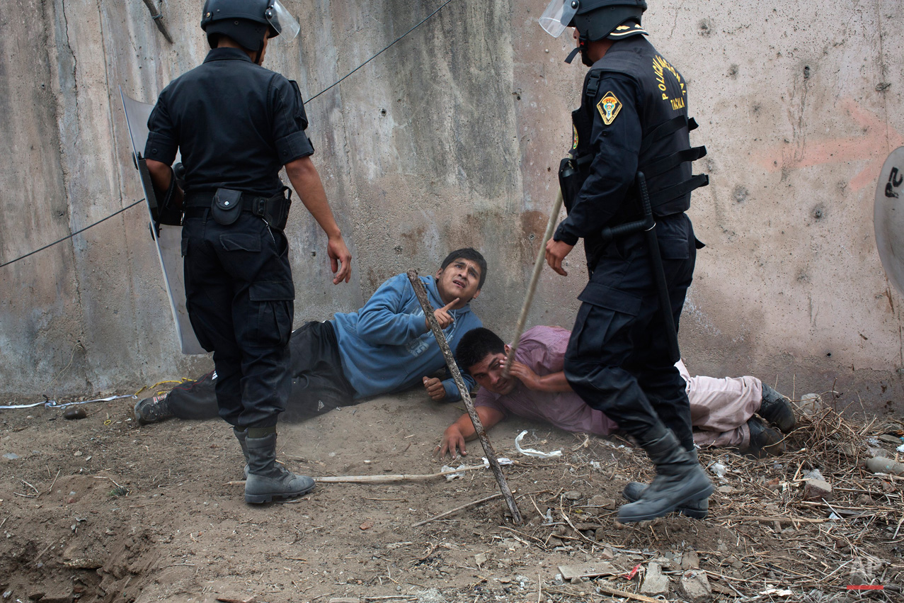 In this May 19, 2015, photo, riot police detain men during a land eviction in Lima Peru. On Monday hundreds of people squatted on land that according to the Ministry of Culture is an archaeological site. (AP Photo/Rodrigo Abd)