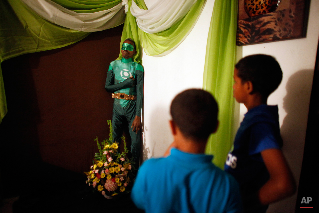 In this Feb. 15, 2015, photo, two boys attend the wake of Renato Garcia, dressed as fictional superhero the Green Lantern and propped up against a wall in his sister's apartment, in San Juan, Puerto Rico. Garcia's sister explained that she and her brother never discussed funeral wishes, but neighbors and friends suggested dressing him as the comic book superhero. (AP Photo/Ricardo Arduengo)