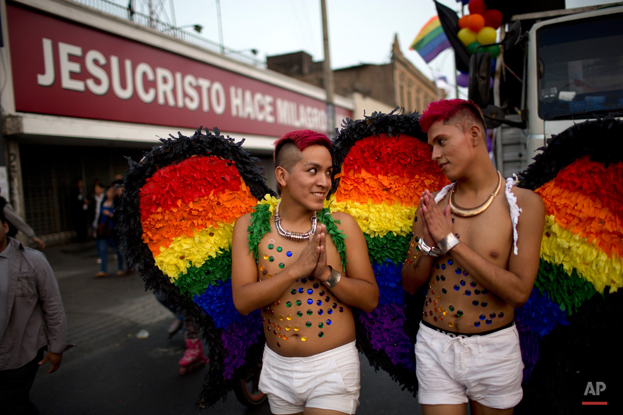 In this June 27, 2015, photo, two young men wearing rainbow colored wings march in the annual gay pride parade, past an evangelical church with a sign that reads in Spanish; "Jesus Christ does miracles," in Lima, Peru. (AP Photo/Rodrigo Abd)