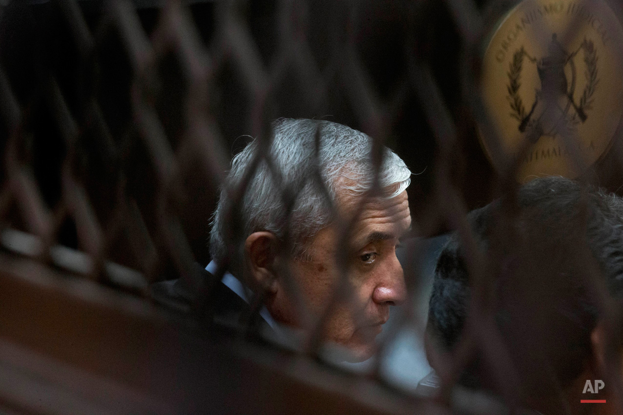 In this Sept. 8, 2015, photo, Guatemala's former president Otto Perez Molina, photographed through a window, sits in court for a third hearing on corruption allegations that led him to resign, in Guatemala City. The court is considering allegations that Perez Molina was involved in a scheme in which businesspeople paid bribes to avoid import duties through Guatemala's customs agency. (AP Photo/Esteban Felix)