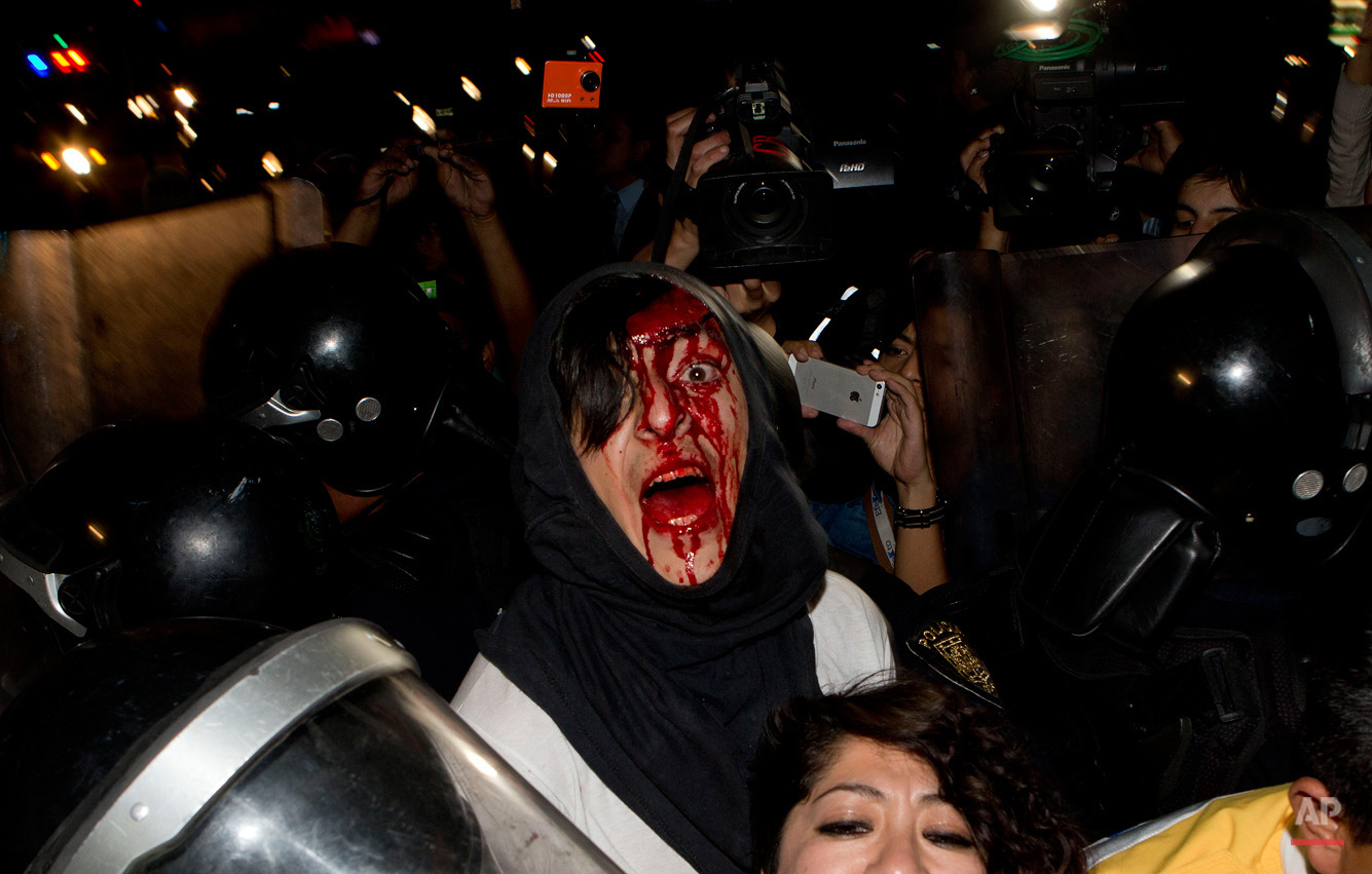 In this Feb. 26, 2015, photo, a protester injured in a scuffle with police shouts out his name as he and a woman are detained in Mexico City. The pair, and other protesters who had taken part in a march marking the fifth month of the disappearance of 43 students from a rural teachers college, clashed with police after they were prevented from entering the subway. (AP Photo/Eduardo Verdugo)