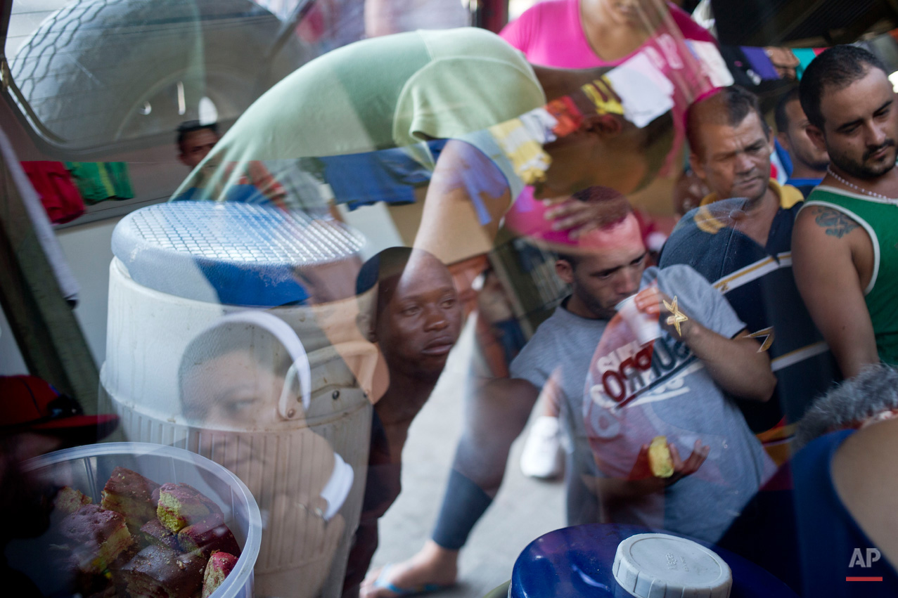 In this Nov. 17, 2015, photo, Cuban migrants are reflected in the window of a nun's jeep, as they gather round for free breakfast items, near the immigration office in PeÒas Blancas, Costa Rica. More than 1,000 Cuban migrants heading north to the United States tried to cross the border from Costa Rica into Nicaragua, causing tensions to soar between the neighbors as security forces sought to turn them back. Nicaragua's government responded furiously on Sunday with a statement saying that Costa Rica "had deliberately and irresponsibly thrown, and continues to throw" the Cuban migrants into its territory, violating its national sovereignty. (AP Photo/Esteban Felix)