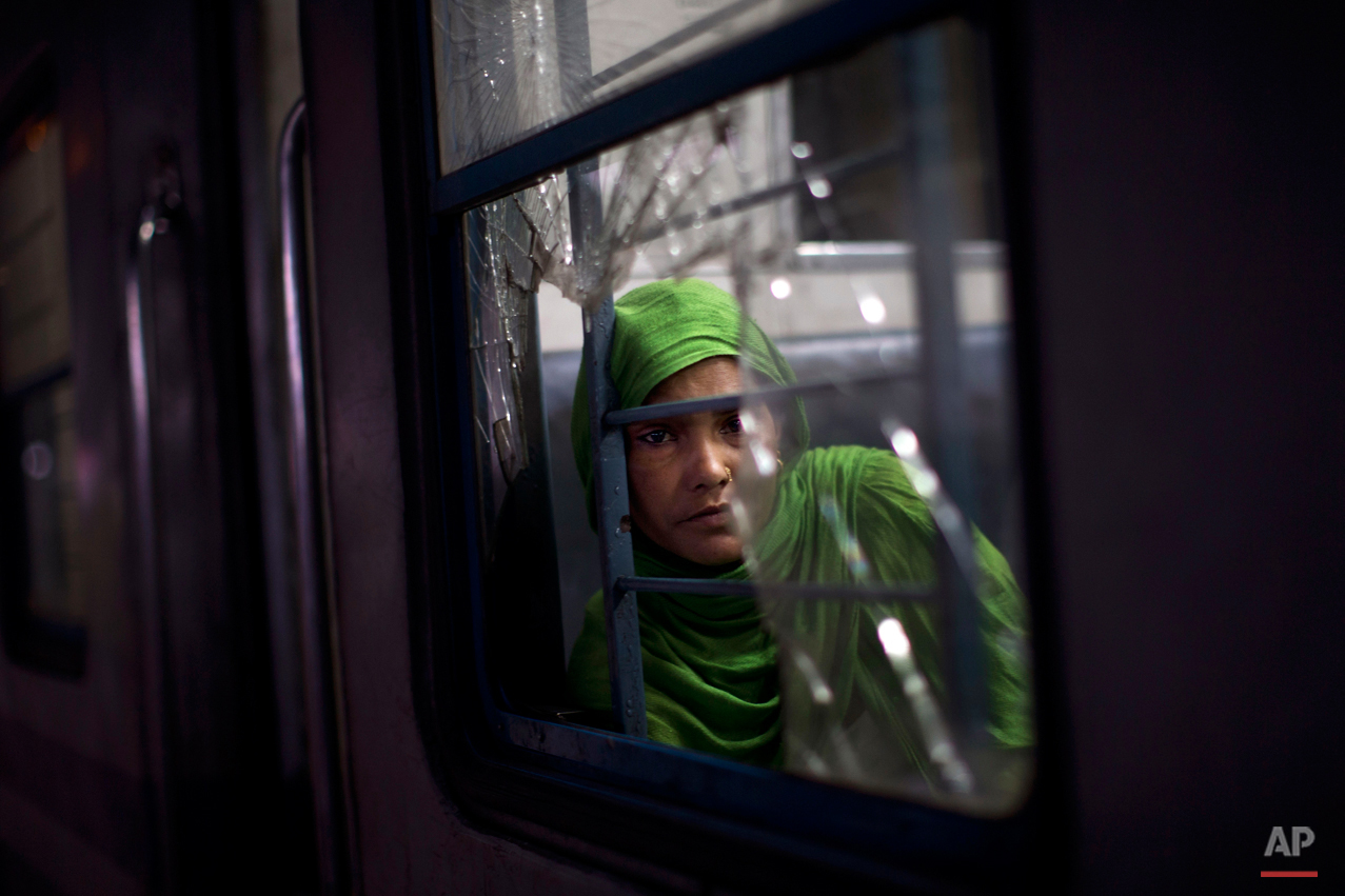  In this Wednesday, Feb. 25, 2015, photo, an Indian woman watches from a broken window of a local train at a railway station in New Delhi, India. India's national railways system, which is one of the world's largest, serves more than 23 million passe