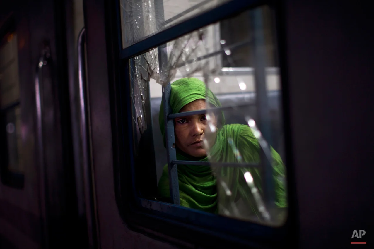 In this Wednesday, Feb. 25, 2015, photo, an Indian woman watches from a broken window of a local train at a railway station in New Delhi, India. India's national railways system, which is one of the world's largest, serves more than 23 million passengers a day. (AP Photo/Bernat Armangue)
