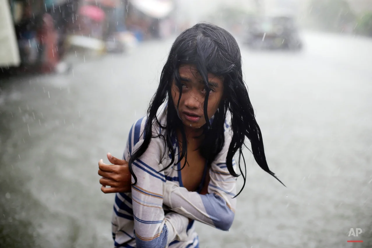 In this Wednesday, July 8, 2015, photo, a Filipino girl tries to keep herself warm as she wades through floodwaters in the coastal village of Malabon, north of Manila, Philippines. Typhoon Chan-Hom passed over the northeastern waters of the Philippines and heading to northern Taiwan on Wednesday, dumping heavy rains over the capital, Manila, and the northern provinces. (AP Photo/Aaron Favila)