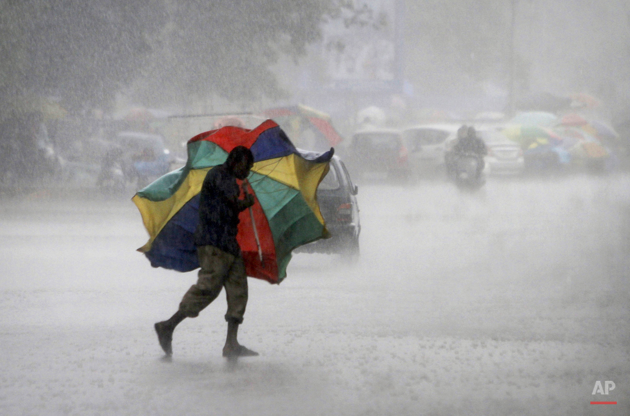  In this Friday, July 3, 2015, photo, a gust of wind bends the umbrella of a street vendor crossing the road during a heavy downpour in the eastern Indian city of  Bhubaneswar, India. (AP Photo/Biswaranjan Rout) 