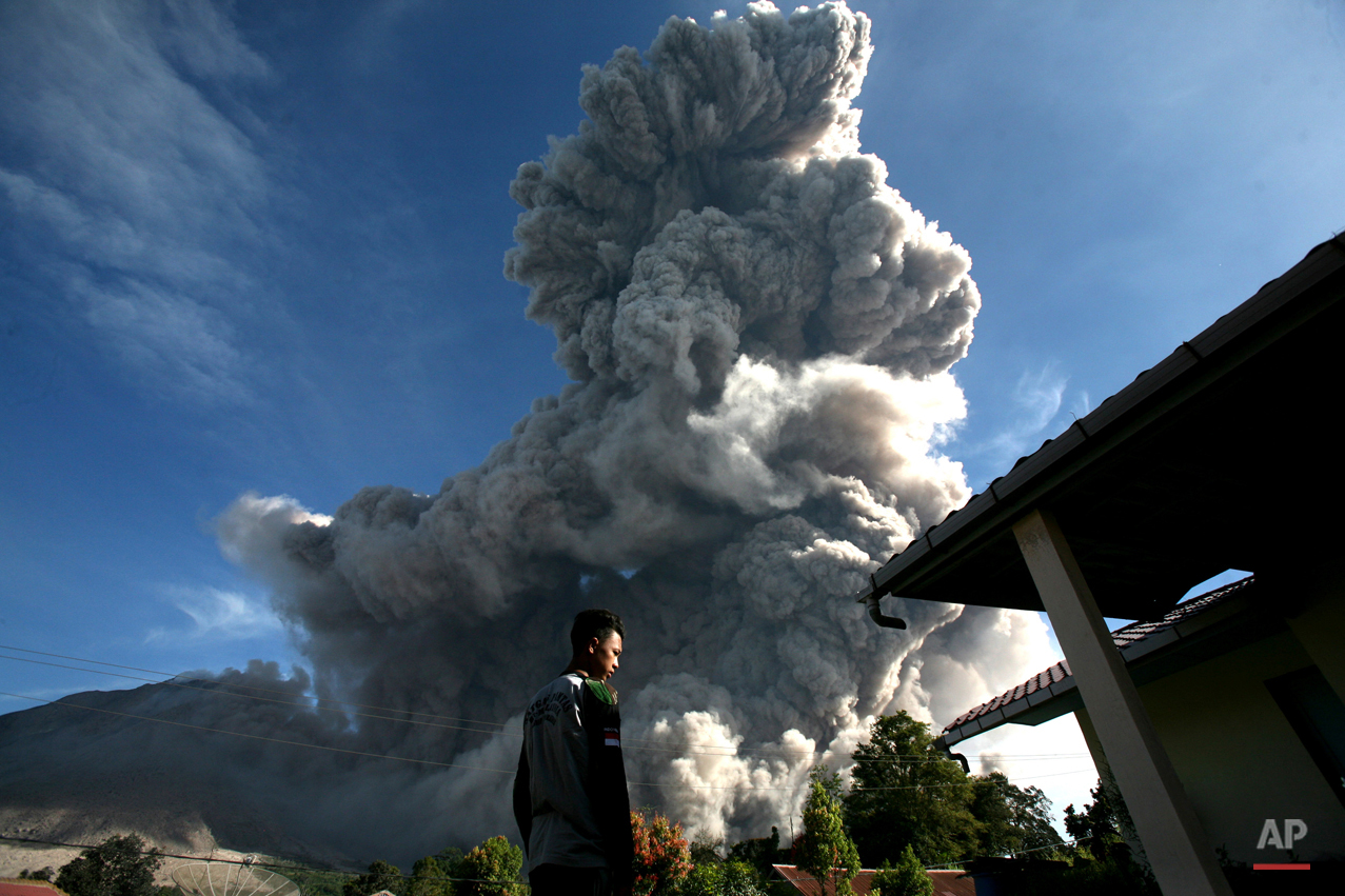  In this Thursday, June 25, 2015, photo, a man watches as Mount Sinabung releases volcanic material into the air in Tiga Serangkai, North Sumatra, Indonesia. The volcano has spewed hot lava almost daily since its alert status was raised early this mo
