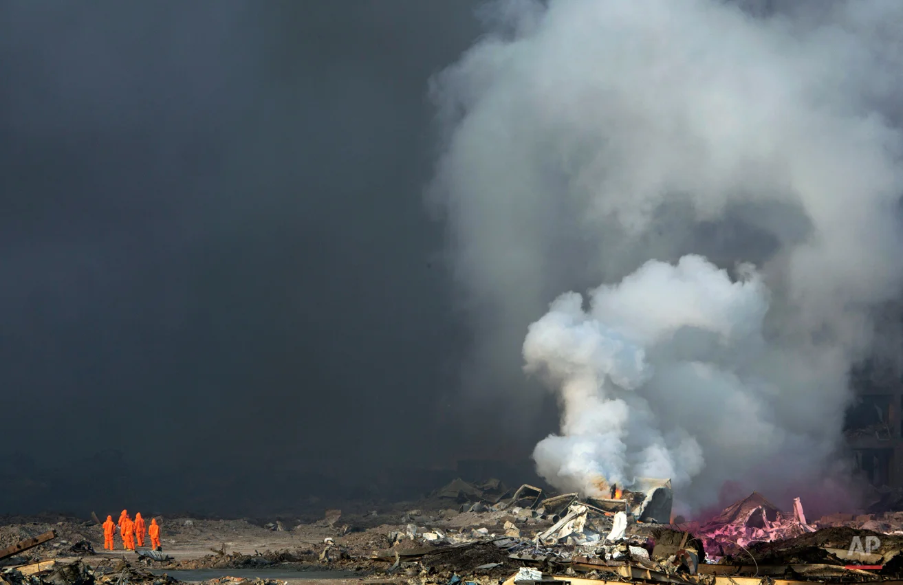 In this Thursday, Aug. 13, 2015 photo, firefighters in protective gear watch as smoke continues to billow out after an explosion at a warehouse in northeastern China's Tianjin municipality. Huge explosions in the warehouse district sent up massive fireballs that turned the night sky into day in the Chinese port city of Tianjin, officials and witnesses said Thursday. (AP Photo/Ng Han Guan)
